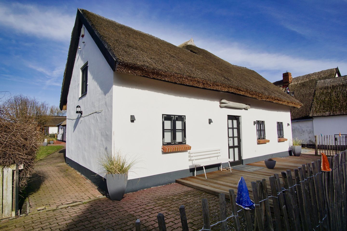 Ein weißes Cottage mit einem Strohdach, einer Holzbank davor und einem Ziegelweg, der zum Eingang führt.
