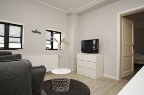 A modern living room with a sofa, a TV on a white dresser, a round coffee table, and a window with a view.
