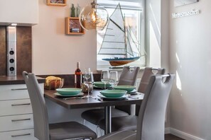 Uma sala de jantar com uma mesa posta para quatro pessoas, com pratos verdes e copos de vinho.