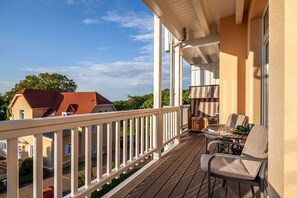 Ein Balkon mit Holzboden, einem Tisch und Stühlen sowie Blick auf benachbarte Häuser.