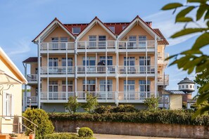 Ein mehrstöckiges Hotel mit Balkonen, einer Steinsäule im Vordergrund und einem Leuchtturm im Hintergrund.