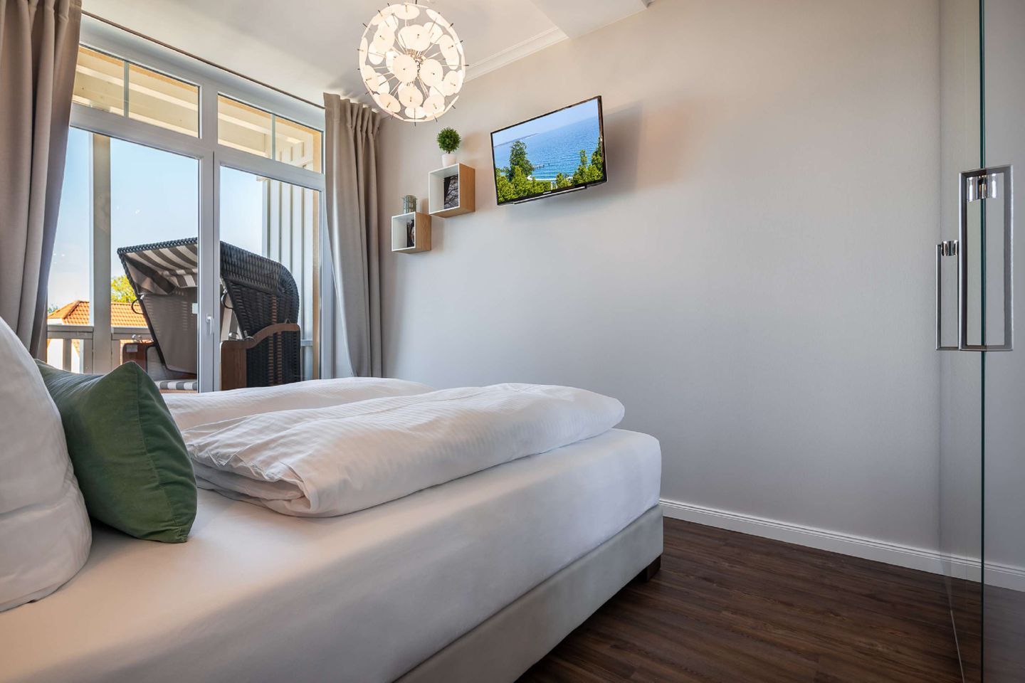 Un dormitorio moderno con una cama grande, un televisor montado en la pared y vista al mar desde la ventana.