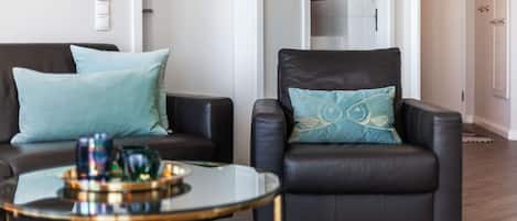 A modern living room with a black leather sofa, a matching armchair, and a glass coffee table with decorative items.