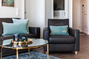 Uma sala de estar moderna com um sofá de couro preto, uma poltrona combinando e uma mesa de centro de vidro com objetos decorativos.