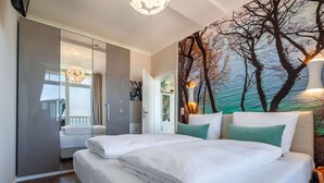 A bedroom with a large bed, a sliding door closet, and a mural of trees and a sunset. - Fantastic sea view from the balcony, use of swimming pool and sauna - Villa Bergfrieden (Göhren)