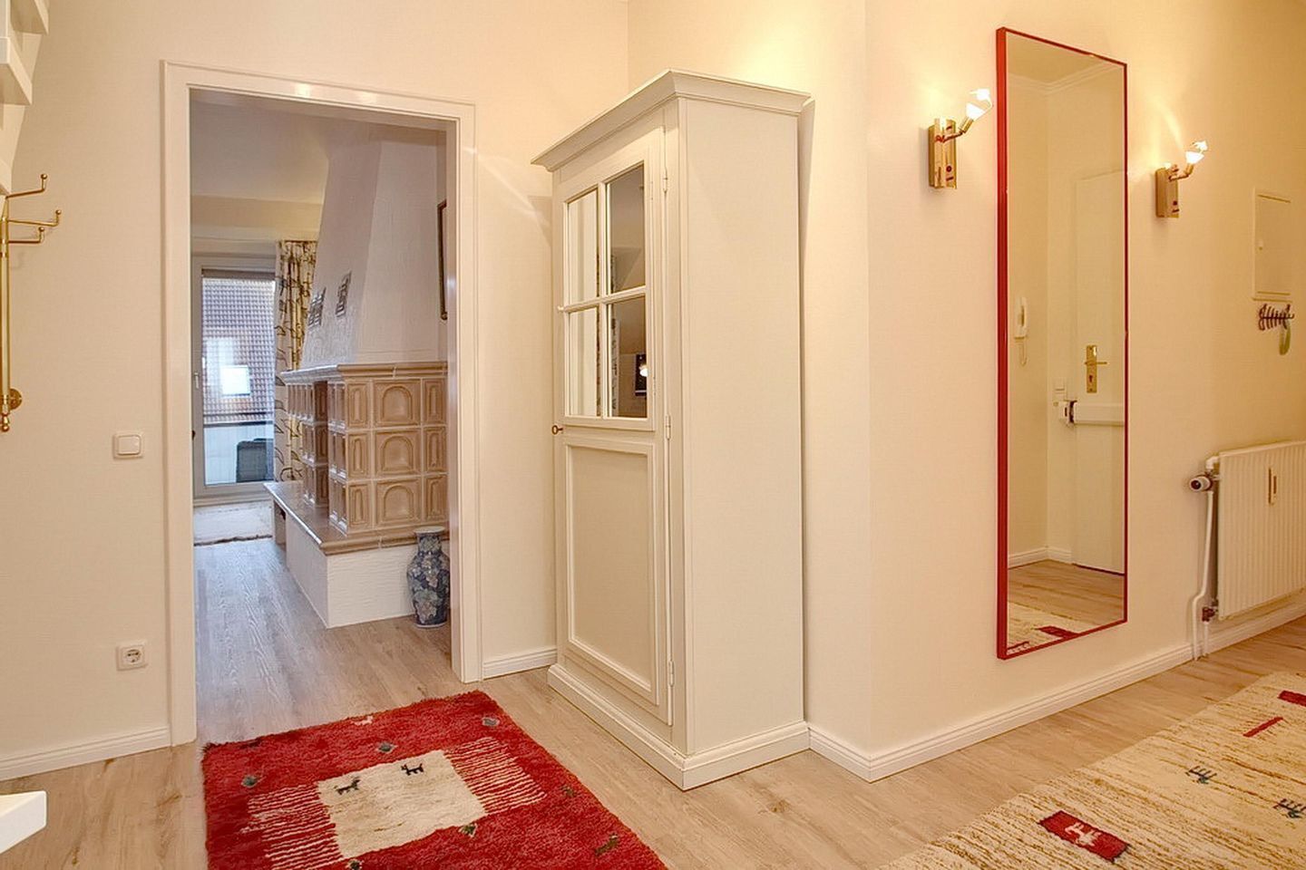 A hallway with a red rug, a white cabinet, and a large mirror.