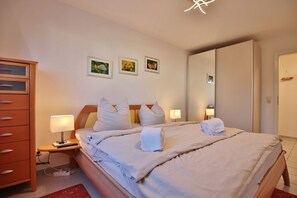 Habitación de hotel con cama, lámparas de noche, cómoda de madera y tres cuadros en la pared.