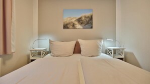 A bedroom with a bed, two bedside tables, a nightstand, and a painting on the wall. - Domizil Strandburg Appartement 5 - Domizil Strandburg (Timmendorfer Strand)