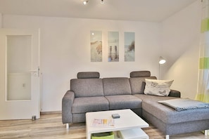 Una sala de estar moderna con un sofá seccional gris, una mesa de centro blanca y tres cuadros en la pared.