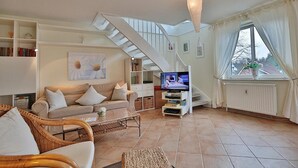 Una sala de estar con un sofá, una mesa de centro y un mueble para el televisor. Se ve una escalera que sube a un piso superior.