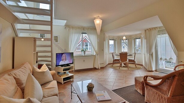 Amplia sala de estar con sofá, televisor y mesa de comedor. Una escalera conduce a un nivel superior.