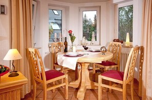 Un coin repas avec une table ronde en bois, des chaises à coussins rouges et une nappe blanche.
