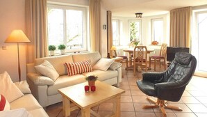 Una sala de estar con un sofá, una mesa de centro, un sillón de cuero negro y un comedor con mesa y sillas.
