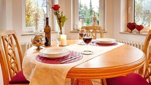 Una mesa de comedor dispuesta con platos, vasos y una vela, rodeada de sillas de madera con cojines rojos.