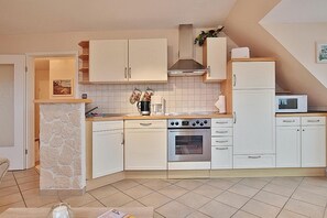 Una cocina compacta con armarios blancos, estufa, horno y microondas.