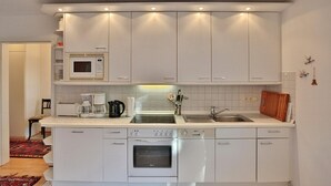 Una cocina compacta con armarios blancos, microondas, cafetera, hervidor y pileta.