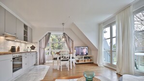 A modern kitchen with a dining area, large windows, and a TV. - Am Elchgrund Apartment 12 - Im Brook 36-38 (Timmendorfer Strand)