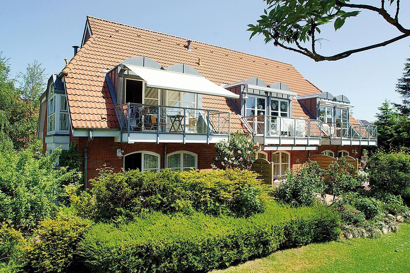 Een herenhuis met een rood pannendak, meerdere balkons en een verzorgde tuin.