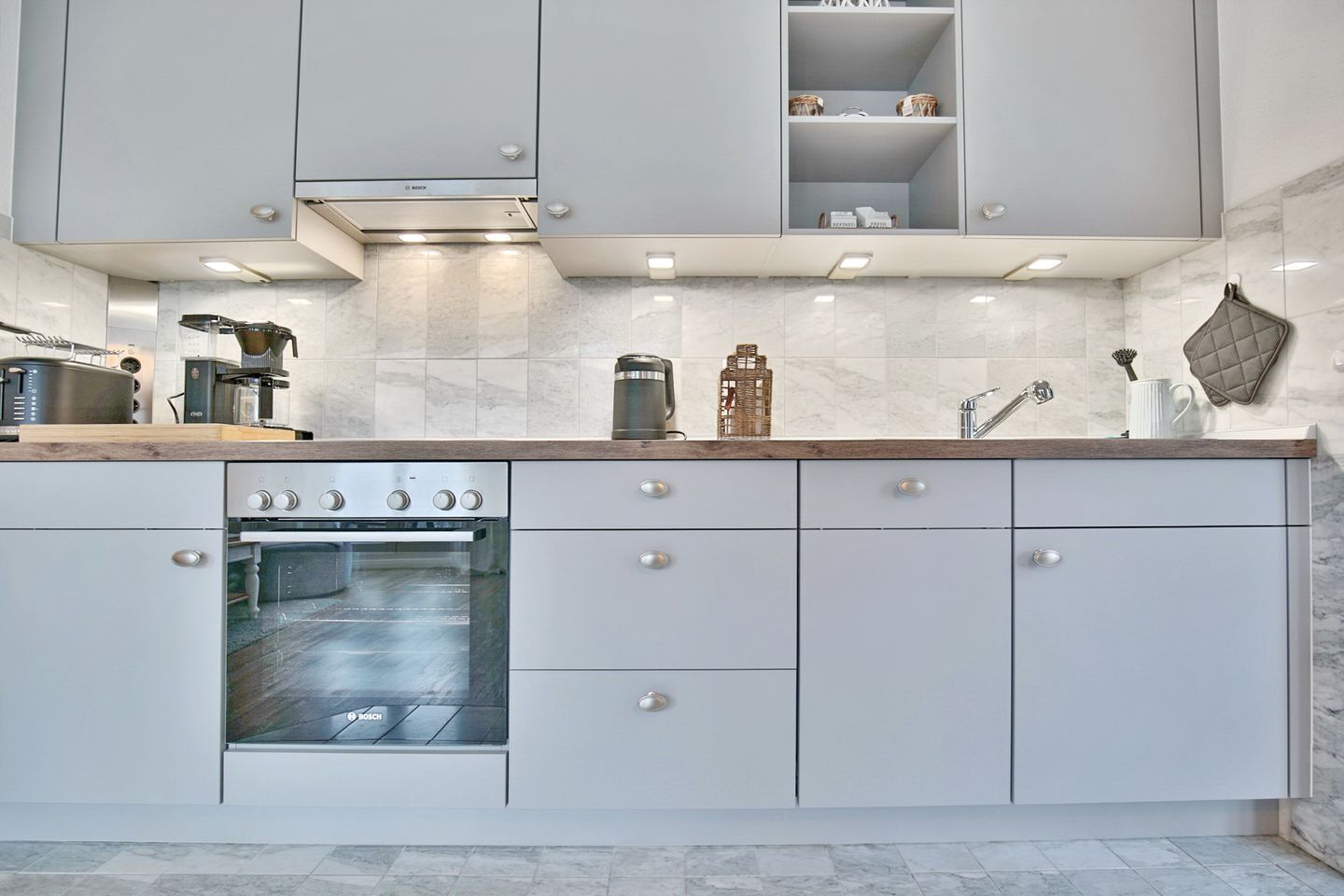 A modern kitchen with white cabinetry, a Bosch oven, and a countertop with various appliances and storage.