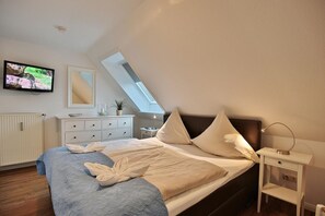 Une chambre à coucher comprenant un lit, une table de chevet, une lampe, un téléviseur, une commode et une lucarne.