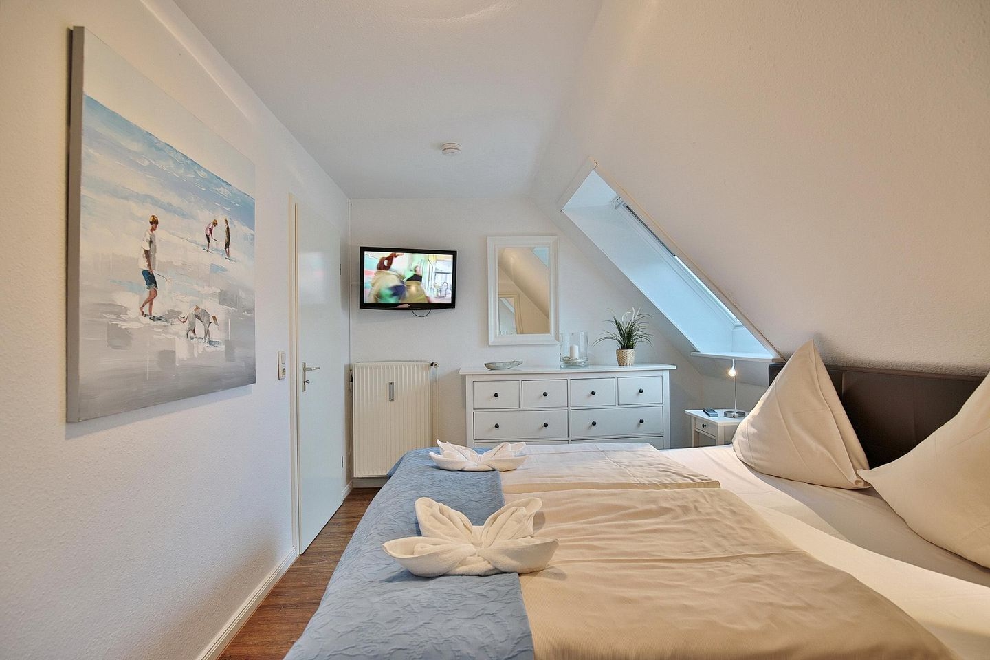 Une chambre à coucher avec un lit, une commode, un téléviseur et une fenêtre de toit.