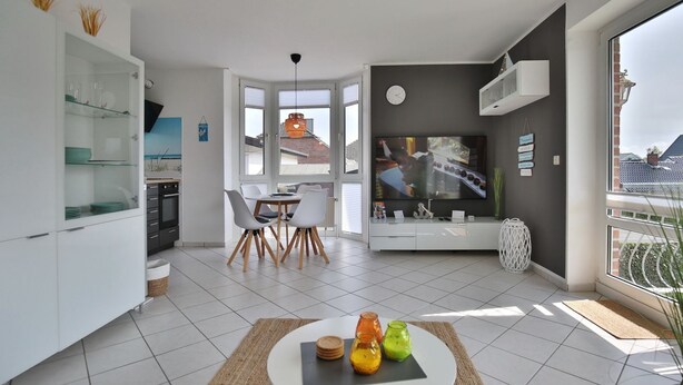 Een moderne woonkamer met een eethoek, grote ramen en een televisie.