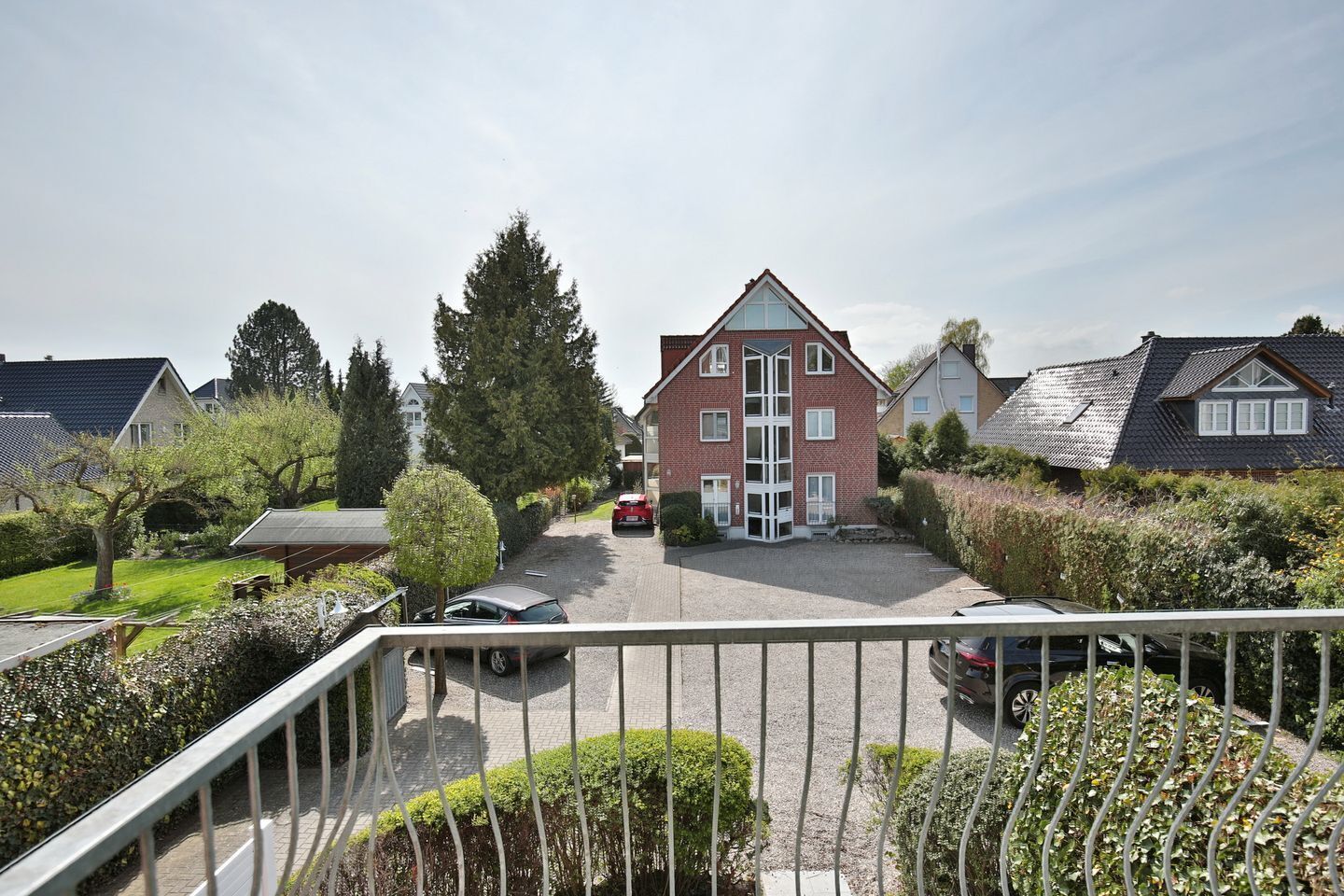 A residential building with a brick facade, a central entrance, and a driveway with parked cars.