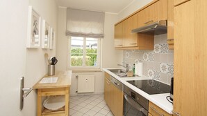 Cocina compacta con armarios de madera, horno empotrado, estufa y ventana con vistas al verdor.