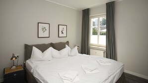 Una cama bien hecha con sábanas blancas, una lámpara de noche y una mesita de madera.