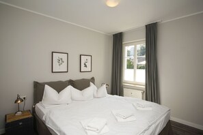 Een keurig opgemaakt bed met witte lakens, een bedlampje en een klein houten nachtkastje.