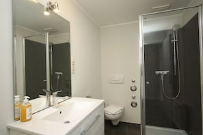 Ein modernes Badezimmer mit weißem Waschbecken, Spiegel und Toilette, sowie einer Duschkabine.