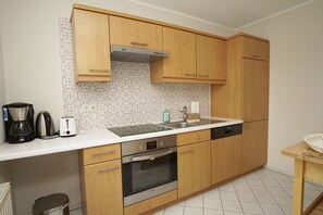 A modern kitchen with wooden cabinets, a stainless steel oven, a dishwasher, and a coffee maker. - Vacation apartment in spa style with conservatory - Villa Maria FeWo Marianne 35 - (Göhren)