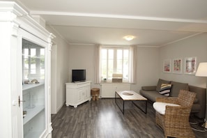 A living room with a television on a cabinet, a sofa, a coffee table, and a wicker chair.