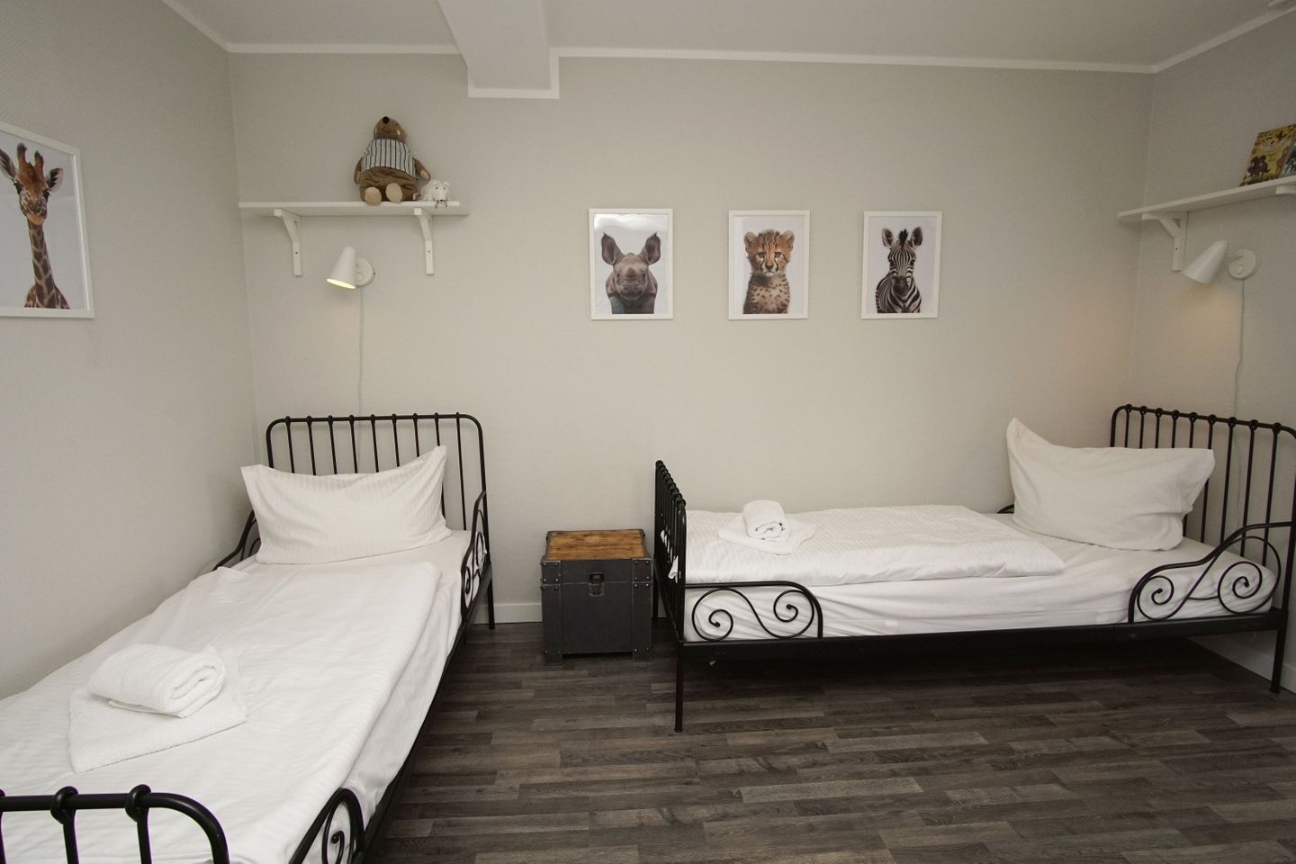 A room with two single beds, a wooden chest, and wall-mounted shelves with animal-themed decorations.