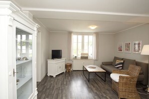 Un salon avec un téléviseur posé sur un meuble, un canapé, une table basse et un fauteuil en osier.