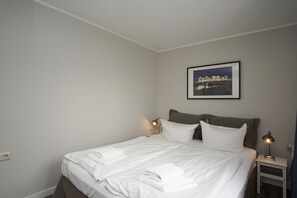 A neatly made bed with white linens and towels, a framed picture on the wall, and two bedside lamps. - Bathroom-style vacation apartment with conservatory - Villa Maria FeWo Maja 36 - Villa (Göhren)