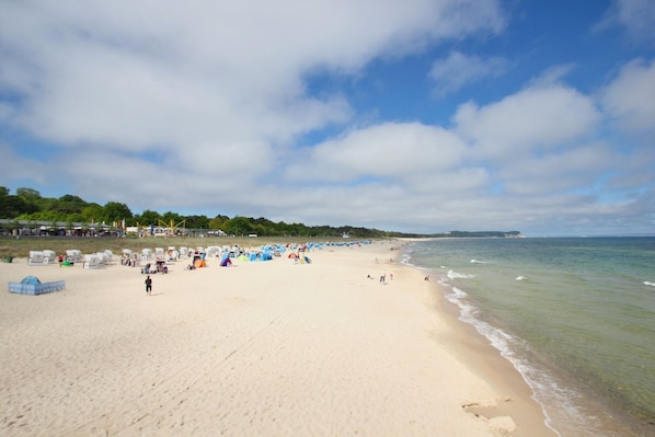 Une vaste plage de sable fin, parsemée de tentes et fréquentée par des baigneurs, un ciel dégagé et une mer calme.