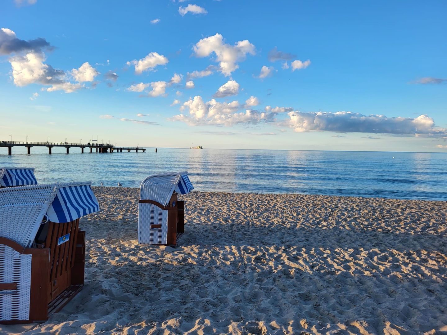 Ein Strand mit zwei Korbstühlen und einer Holzbank.