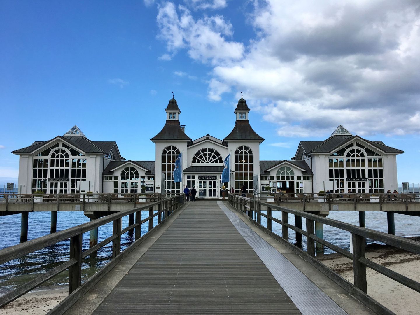 A pier leading to a waterfront building with multiple sections, each with a distinct architectural style.
