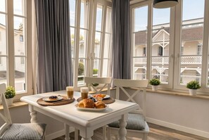 A dining area with a table set for breakfast, including pastries and beverages, with large windows and curtains. - Vacation Apartment with Bathroom and Veranda - Villa Maria FeWo Maja 36 - Villa (Göhren)