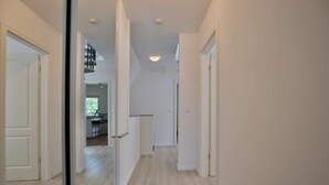 Un pasillo con paredes blancas y suelo de madera que conduce a una zona de cocina con ventanal.