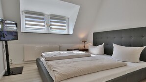 Un dormitorio con una cama grande, televisión, radiador y ventana con persianas.