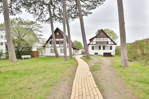 Een pad dat leidt naar een traditioneel herenhuis met een witte gevel en donkere accenten, omgeven door bomen en een gazon.