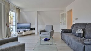 Una sala de estar moderna con un televisor de pantalla plana, un sofá gris, un sillón gris y una mesa de centro de vidrio.