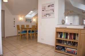 A dining area with a table and chairs, a bookshelf with books and games, and a skylight above the table.