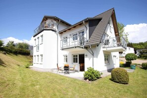 Ein zweistöckiges Haus mit Balkon, einer Terrasse und Gartenmöbeln sowie einem gepflegten Rasen.