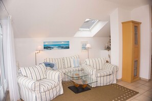 Ein Wohnzimmer mit zwei gestreiften Sofas, einem Glastisch, einem Strandbild, einer Lampe und einem Holzschrank.
