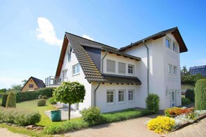 Ein zweigeschossiges Haus mit einem geneigten Dach, zahlreichen Fenstern und einem gepflegten Garten mit verschiedenen Pflanzen und Blumen.