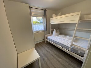 A bunk bed room with a window, radiator, and a small table.