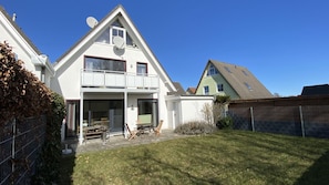 A two-story house with a balcony, a patio with outdoor furniture, and a fenced yard. - Vacation apartment in a quiet location with a balcony - Ferienhaus Solamar FeWo OG - (Breege)